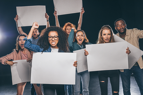 young multicultural people screaming while holding blank placards on black