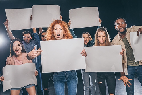 young multicultural people screaming while holding empty boards on black