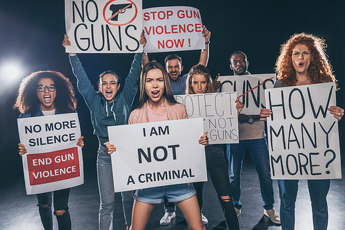 emotional multicultural people screaming while holding placards on black