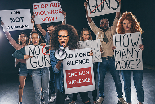 emotional african american girl screaming in megaphone near people holding placards on black