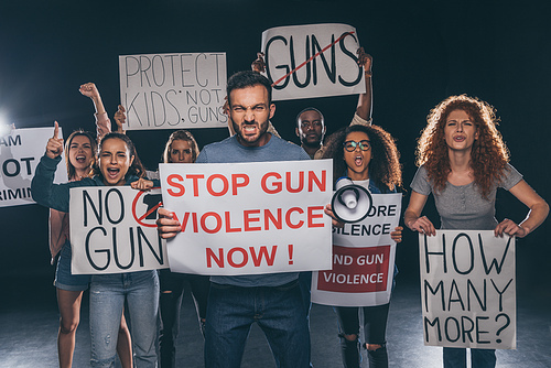 angry man holding placard with stop gun violence now lettering near multicultural people on black
