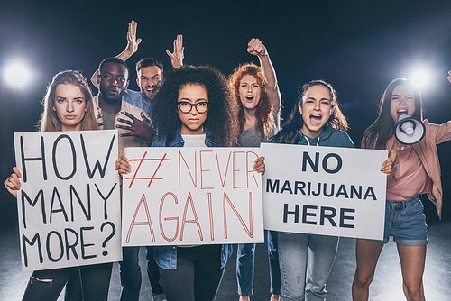 emotional multicultural people screaming while holding placards with lettering on black