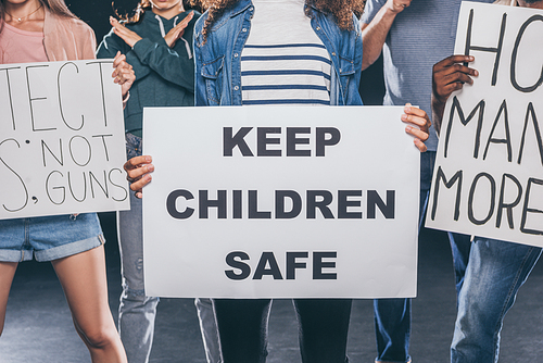 cropped view of woman holding placard with keep children safe lettering near group of people on black