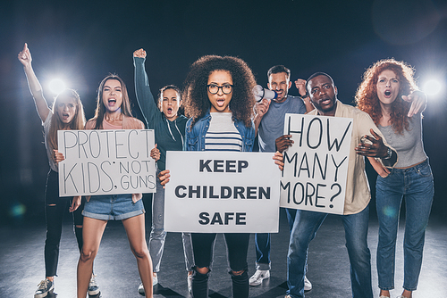 emotional african american woman holding placard with keep children safe lettering near group of people on black