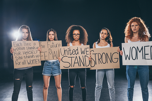 attractive multicultural women standing and holding placards on black