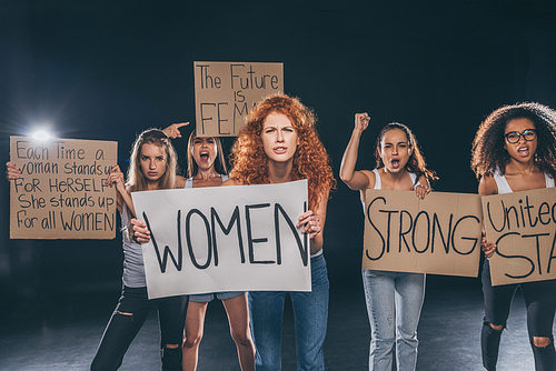 emotional multicultural women standing and holding placards on black