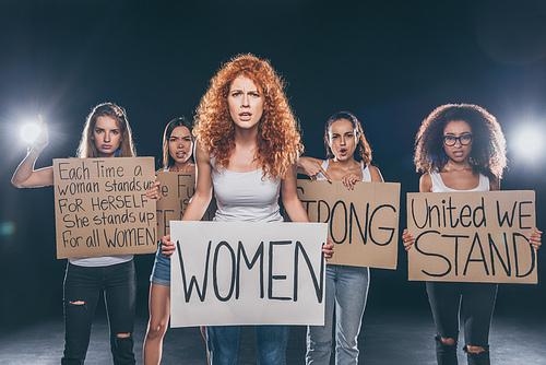 attractive multicultural girls standing and holding placards with lettering on black