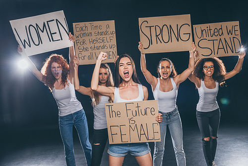 emotional multicultural women screaming and holding placards on black