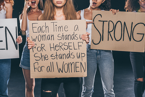 cropped view of multicultural women standing and holding placards on black