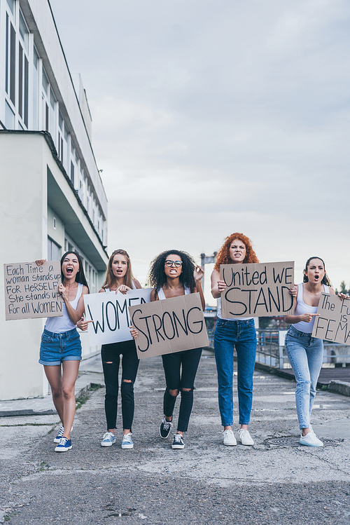 emotional multicultural girls holding placards and screaming near building