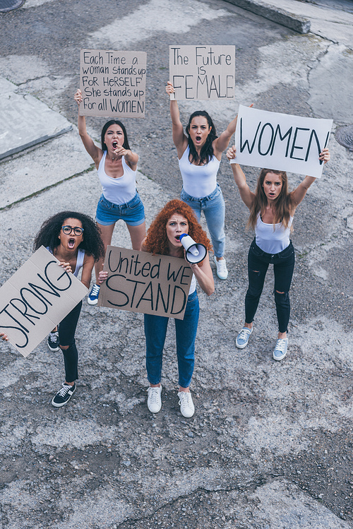 overhead view of emotional multicultural girls holding placards and screaming outside