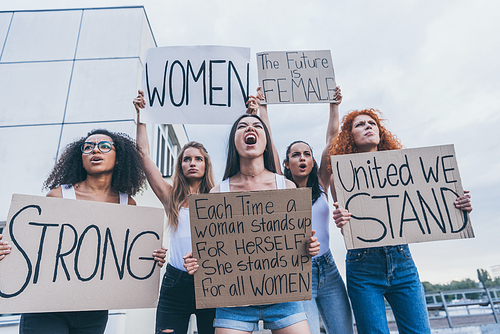 low angle view of multicultural women holding placards and screaming outside