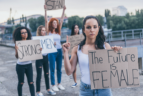 selective focus of attractive girl pointing with finger while holding placard with the future is female letters