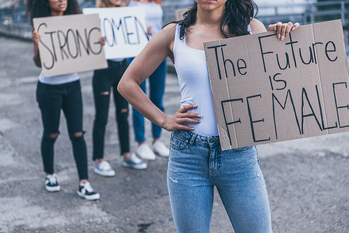 cropped view of girl holding placard with the future is female letters while standing with hand on hip