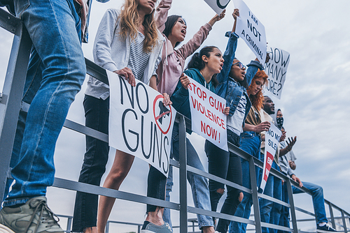 cropped view of multicultural people with lettering on placards screaming near river