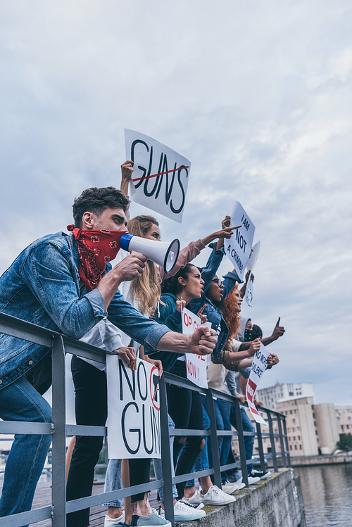 emotional man with scarf on face gesturing and holding megaphone near multicultural people with placards