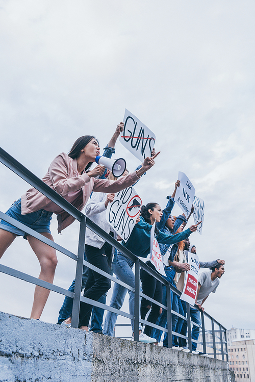 low angle view of girl with megaphone screaming with group of multicultural people holding placards