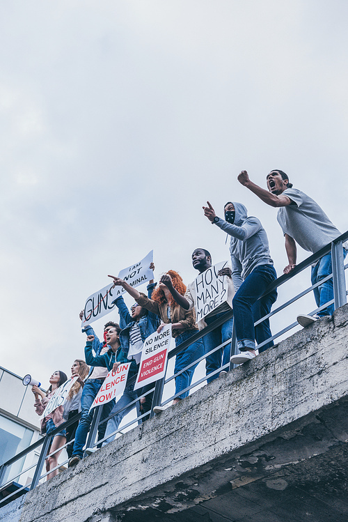 low angle view of multicultural group of people screaming and gesturing while holding placards