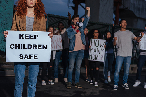 cropped view of redhead girl holding placard with keep children safe lettering near multicultural people on meeting
