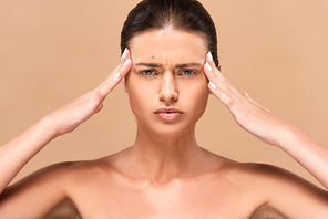 focused and naked woman with pimple on face touching temples isolated on beige