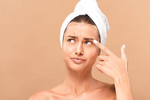 displeased woman pointing with finger at face with pimple isolated on beige