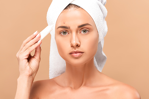 naked girl in towel holding treatment cream near face with problem skin isolated on beige