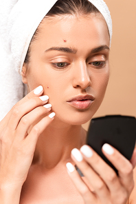 selective focus of woman touching face with pimples and looking at mirror isolated on beige