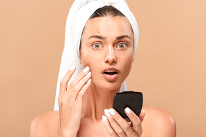 shocked naked woman holding mirror and touching face with pimples isolated on beige