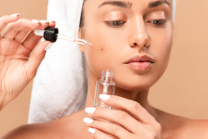 young naked woman applying serum on face with pimples isolated on beige