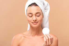 smiling naked girl with acne on face looking at cotton pad isolated on beige