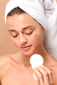 naked girl with acne on face looking at cotton pad isolated on beige