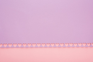 top view of violet paper with cut out hearts on pink background