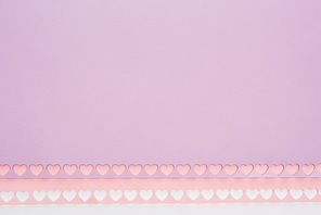 top view of pink, violet paper with cut out hearts on white background