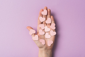 cropped view of woman holding pink paper hearts on violet background