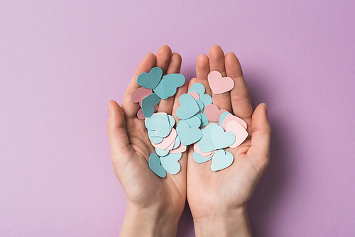 cropped view of woman holding colorful paper hearts on violet background