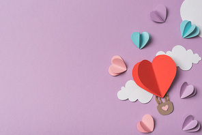 top view of colorful paper hearts and clouds around heart shaped paper air balloon on violet background