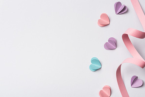 top view of small paper hearts and pink paper swirl on white background