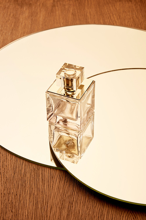 Glass perfume bottle on round beige mirror surface