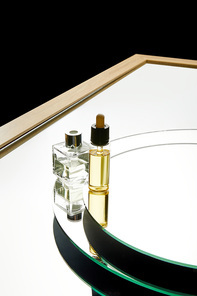 High angle view of aromatic perfume bottle and serum bottle on mirror surface isolated on black