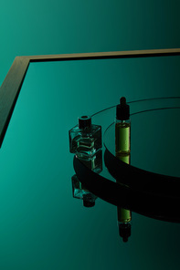 High angle view of perfume bottle and serum bottle on dark green mirror surface