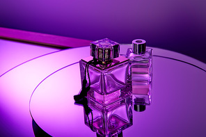 Purple glass perfume bottles on round violet mirror surface with reflection