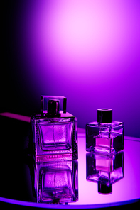 Violet perfume bottles on round mirror surface and light spot on background