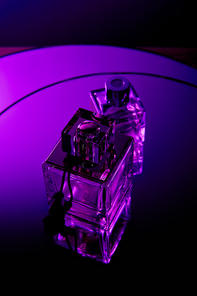 Top view of perfume bottles on dark dramatic violet round mirror surface