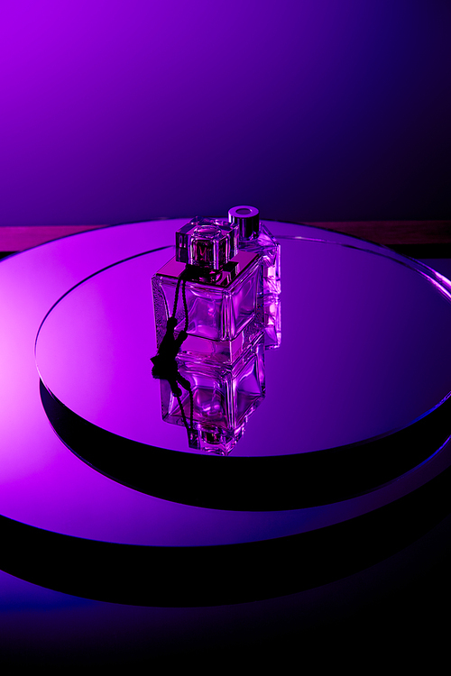 Violet perfume bottles on round mirror surface isolated on purple