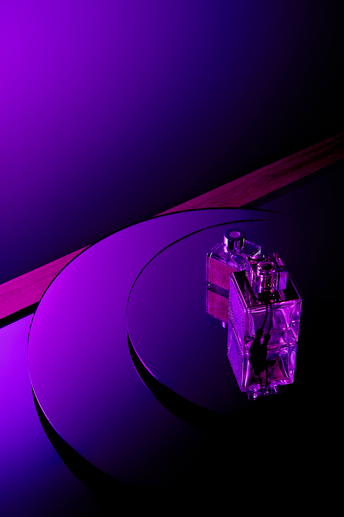 Purple perfume bottles on round mirror surface with dark violet background