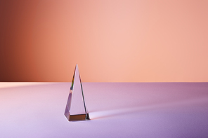 crystal transparent pyramid with light reflection on violet and orange background