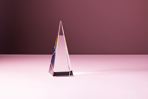 crystal transparent pyramid with light reflection on pink background