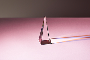 crystal transparent pyramid with light reflection on pink surface