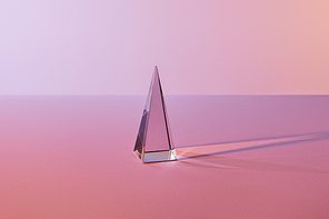 crystal transparent pyramid with light reflection on pink background