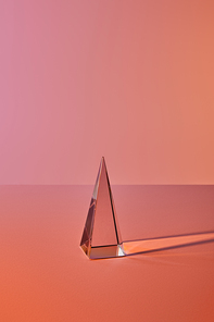 crystal transparent pyramid with light reflection on orange background